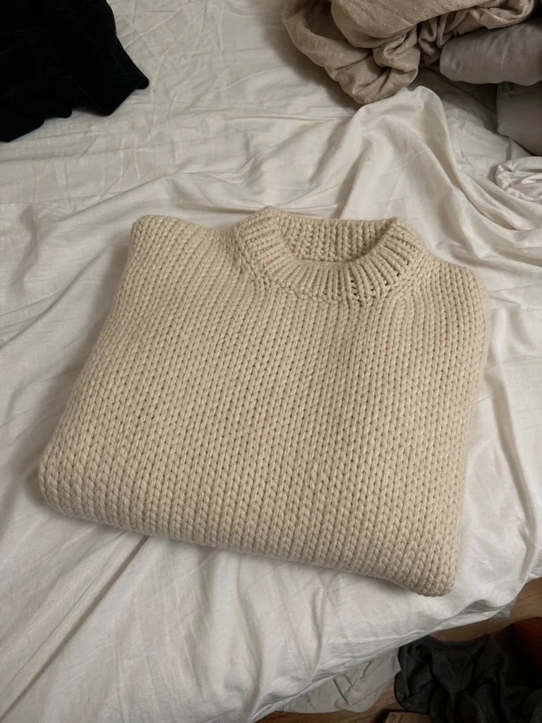 Ton pull tricoté main, pris au téléphone : plié sur un lit défait