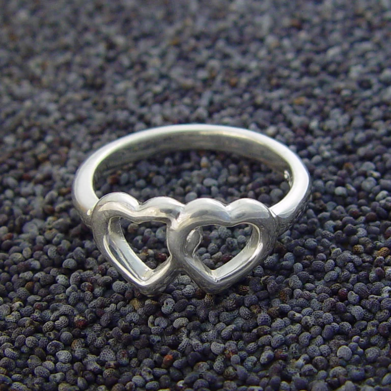 La photo de départ : une bague en argent à deux cœurs ajourés, posée sur des graines de pavot