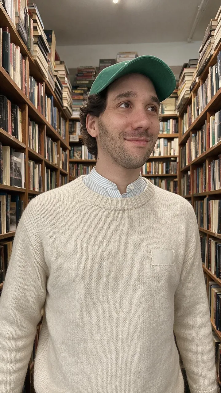 La retouche de la libraire&nbsp;: Ismael entre les rayons d'une librairie, en pull en maille écrue, avec la pose et le cadrage de sa photo